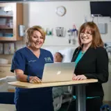 A nurse and nurse leader smile and stand together.